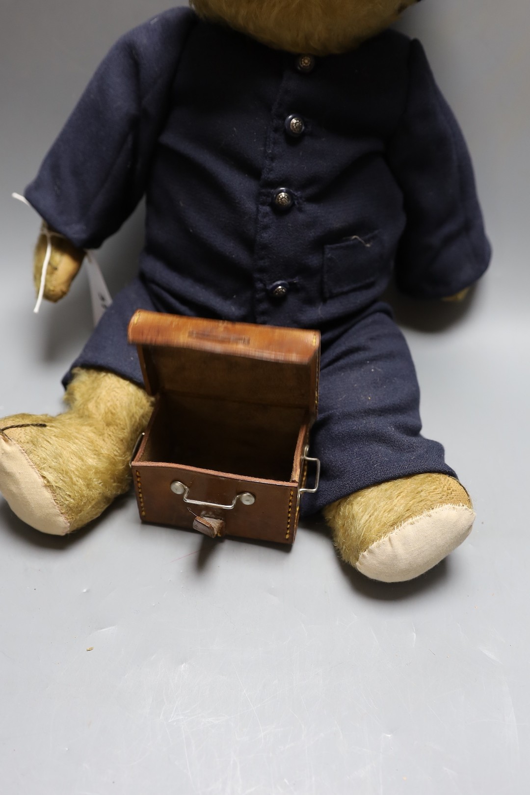 A Chiltern teddy bear dressed as railway porter, replaced footpads, thinning of mohair to tummy and arms together with miniature leather trunk